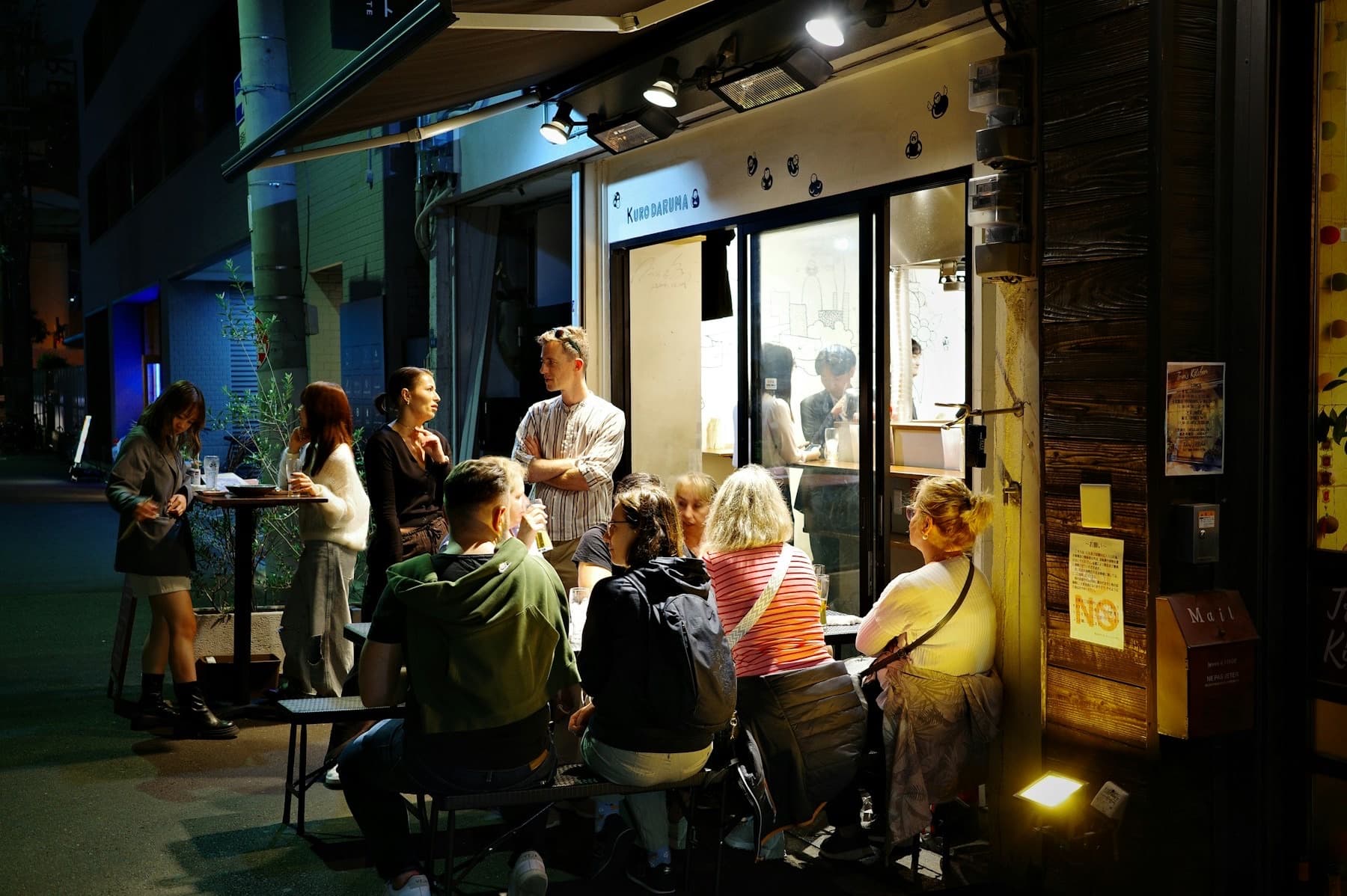 People gathered outside a small brightly lit restaurant at night