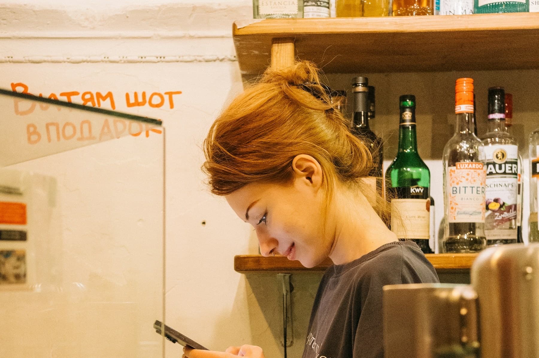 A worker behind a bar counter reading a message on her phone