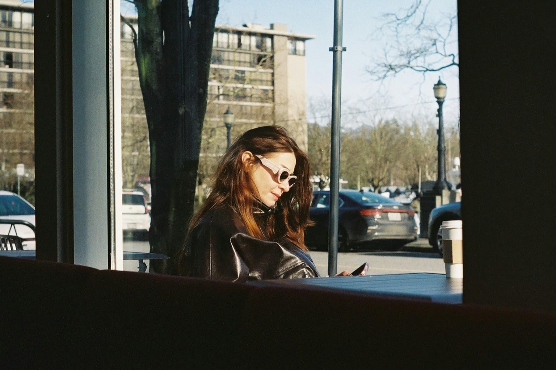 Customer looking at her phone inside a cafe, street visible outside